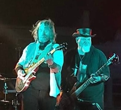 Two guitarists performing on stage under teal lights
